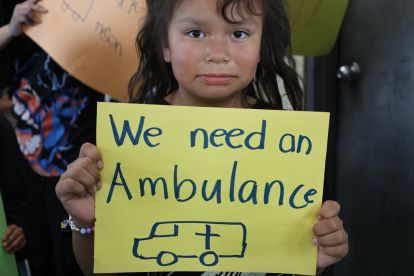 A young resident of Neskantaga holding a sign that says “We need an ambulance”