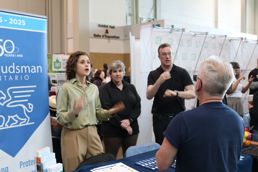 Staff person, alongside ASL interpreter, speaking to person at event
